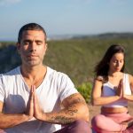 Man and woman meditating outdoors on yoga mats by the coast in Portugal.