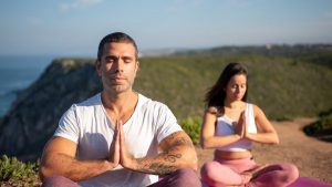 Man and woman meditating outdoors on yoga mats by the coast in Portugal.